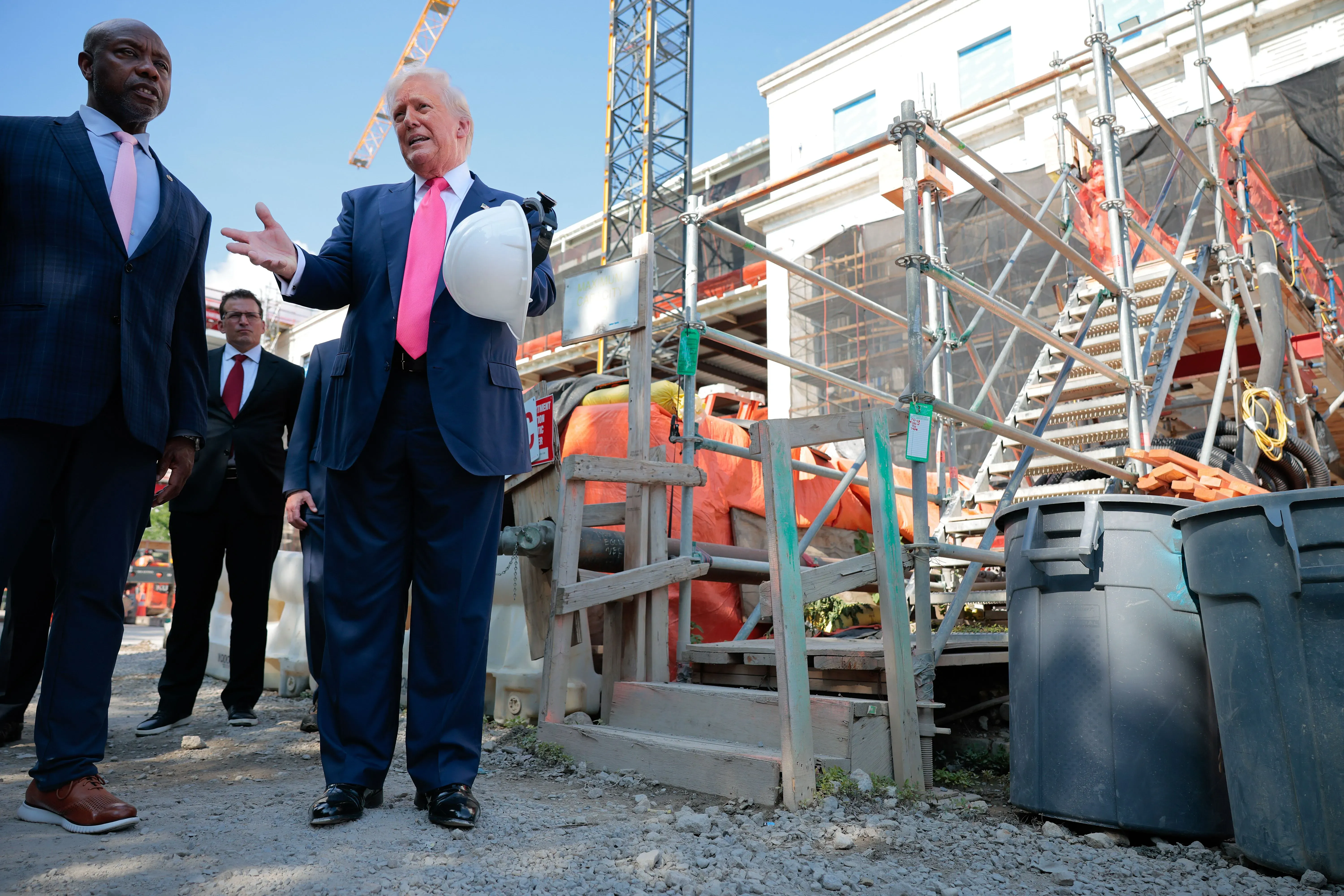 ترامب يتحدث مع مسؤولين أثناء جولة في موقع تجديد مجلس الاحتياطي الفيدرالي، مع معدات البناء في الخلفية.
