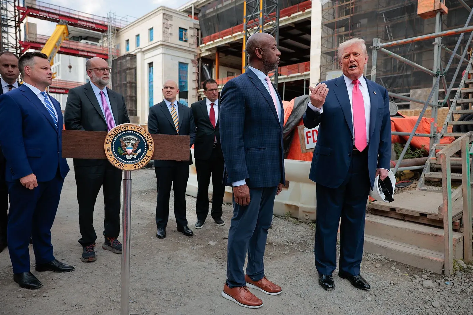 ترامب يتحدث مع جيروم باول وسط مجموعة من المسؤولين في موقع تجديد مجلس الاحتياطي الفيدرالي، مع التركيز على القضايا الاقتصادية.