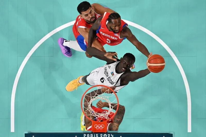 مالواش، لاعب كرة سلة من جنوب السودان، يتنافس في مباراة أثناء محاولته تسجيل نقطة، مع وجود لاعبين من فريق بورتو ريكو يحاولان منعه.