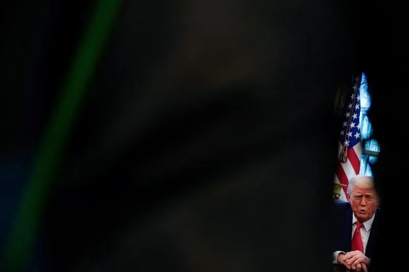 ترامب يجلس في غرفة مظلمة، مع العلم الأمريكي خلفه، في سياق تصاعد التوترات التجارية بين الولايات المتحدة والصين.