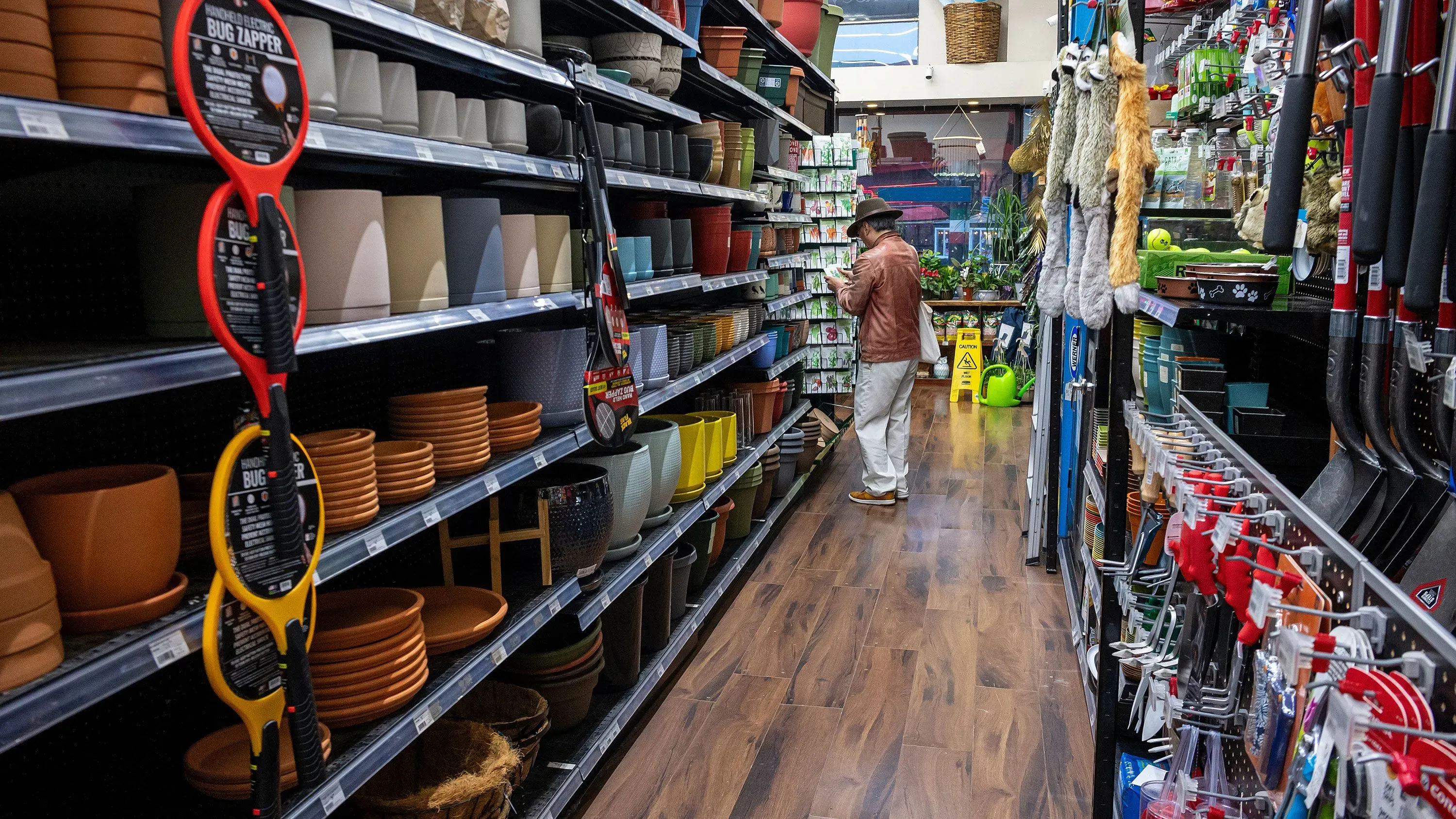 ممر في متجر يُظهر مجموعة متنوعة من أواني الزرع وأدوات الحدائق، فيما يتفقد زبون المنتجات على الأرفف.