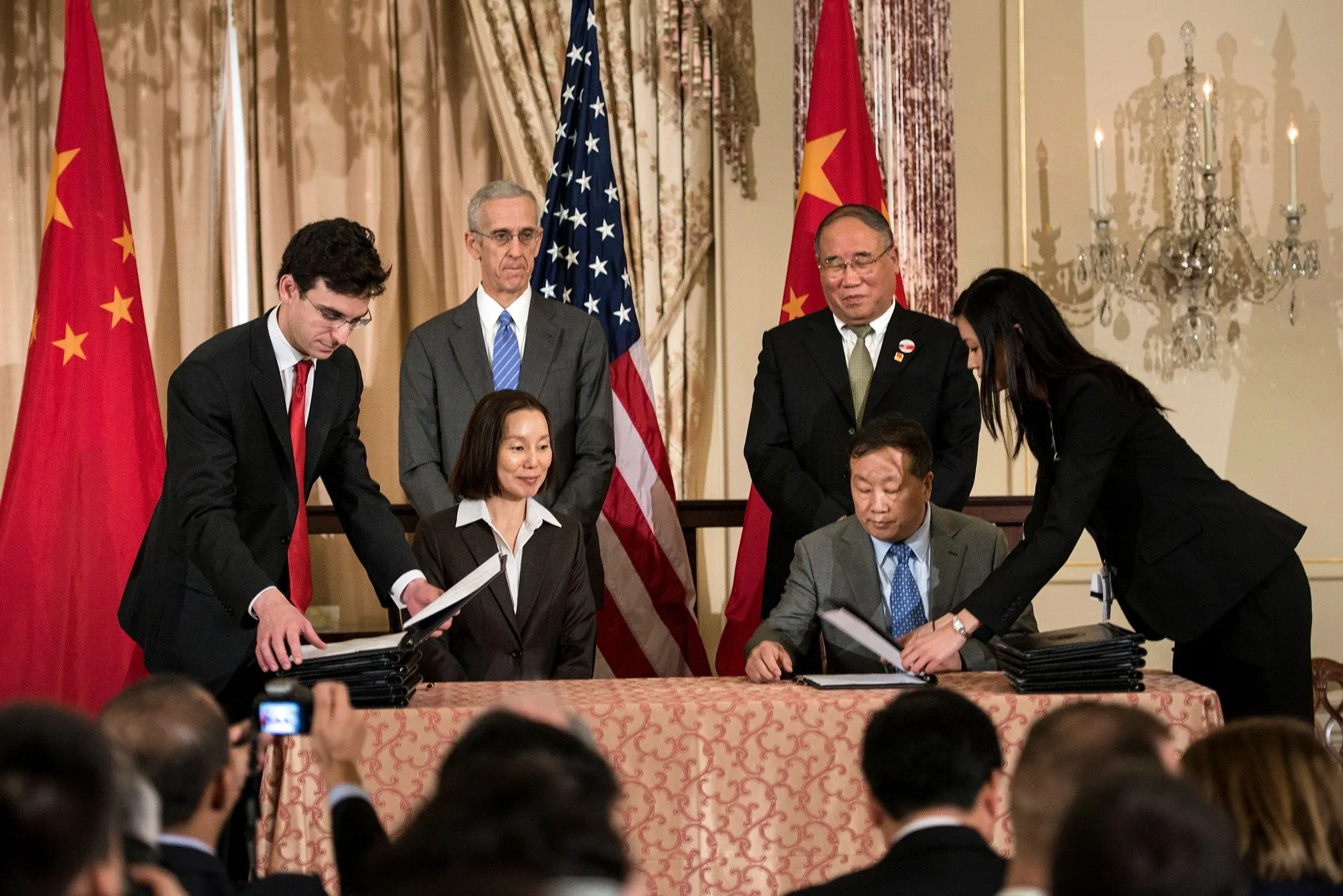 توقيع اتفاقية بين ممثلين عن الولايات المتحدة والصين في إطار التعاون لمواجهة تغير المناخ، مع العلميات الدبلوماسية خلفهم.