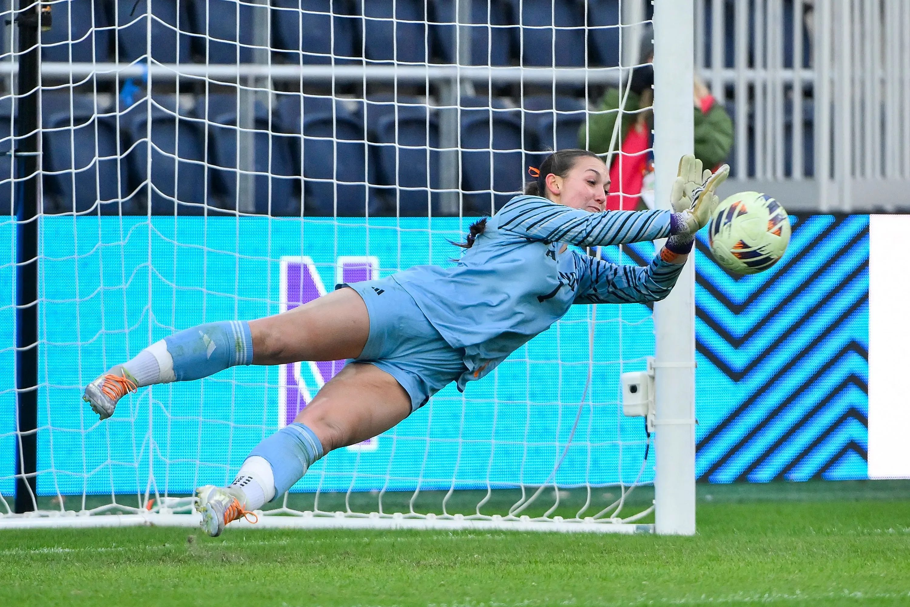 لاعبة كرة القدم ميا هامانت ترتدي زي حارس المرمى، وهي تتصدى لكرة في لحظة حماسية خلال مباراة. خلفها، يظهر الشبك.