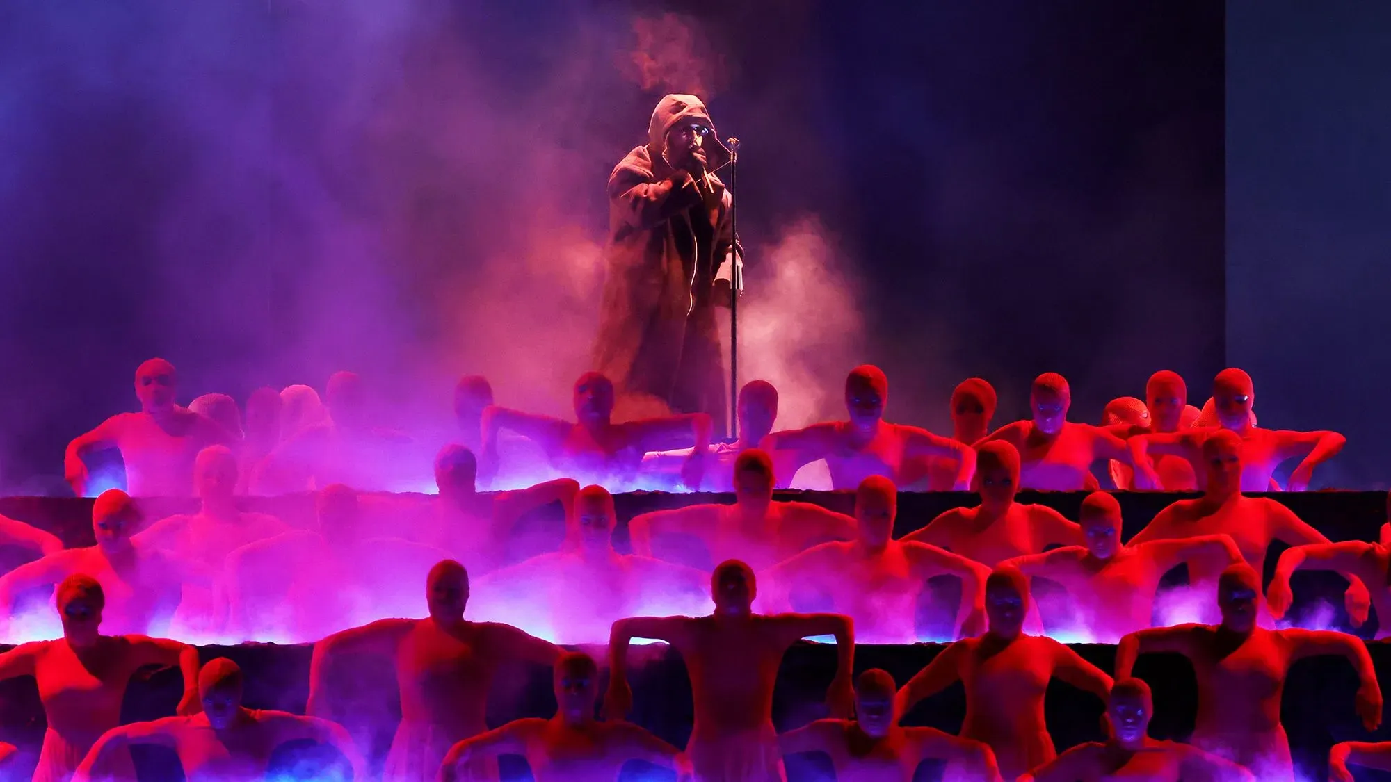 ذا ويكند يؤدي على المسرح محاطًا بفنانين يرتدون زيًا أحمر، مع أضواء ملونة ودخان يضيفان جوًا دراميًا.