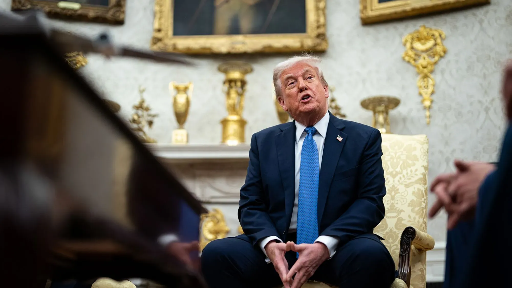 ترامب يتحدث خلال اجتماع في المكتب البيضاوي، مع تفاصيل فاخرة تحيط به، مع التركيز على قضايا الاقتصاد والتعريفات الجمركية.