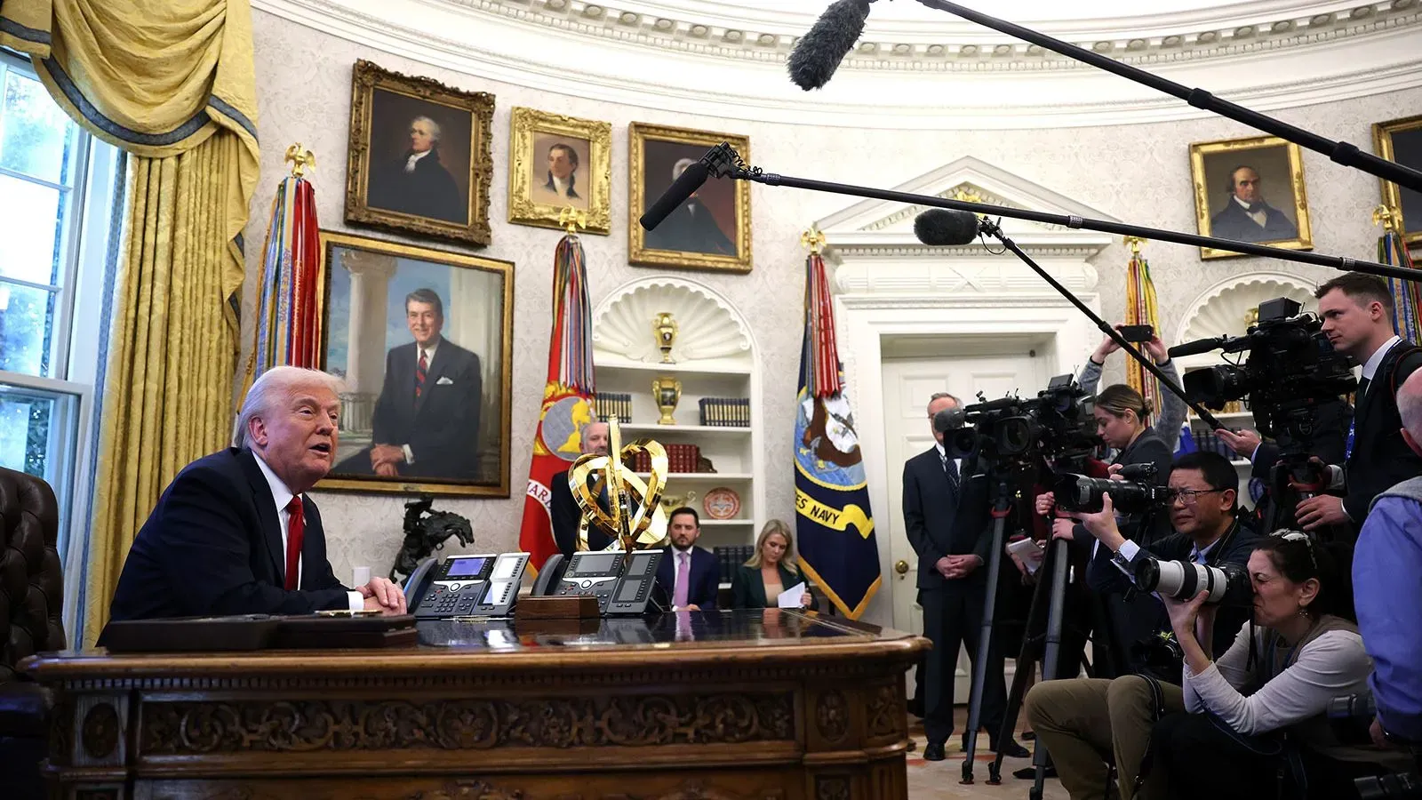 ترامب يجلس في المكتب البيضاوي محاطًا بالصحفيين والكاميرات، مع وجود لوحات تاريخية خلفه، أثناء مؤتمر صحفي حول الأمن القومي.