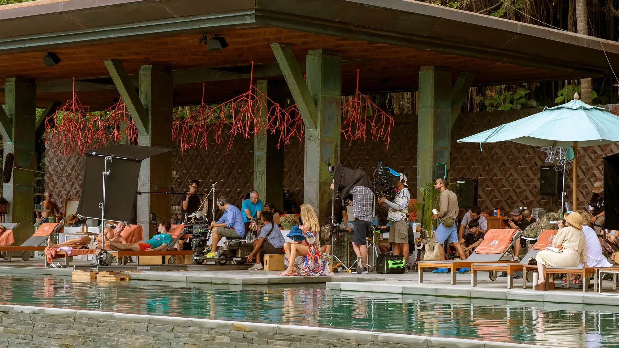 مجموعة من طاقم تصوير مسلسل "اللوتس الأبيض" أثناء العمل بجوار المسبح، مع إعدادات تصوير ومشاهدين في خلفية المكان.