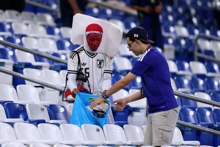 مشجعان في ملعب كرة قدم ينظفان المقاعد بعد المباراة، تعبير عن المسؤولية البيئية في فعاليات كأس العالم 2026.