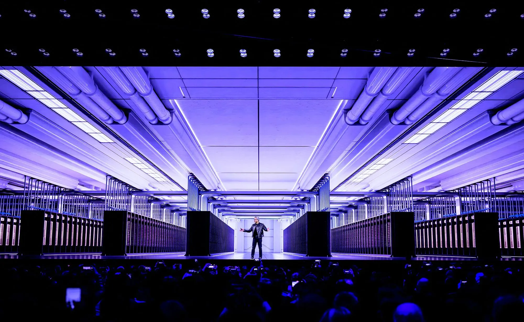 مؤسس إنفيديا، جينسن هوانج، يتحدث في مؤتمر الذكاء الاصطناعي GTC، مع خلفية تكنولوجية متطورة وإضاءة زرقاء.