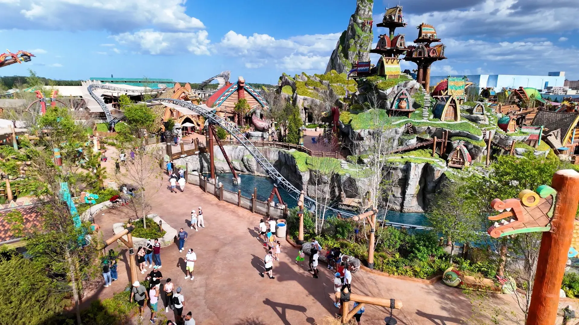 مشهد جوي لمنتزه ترفيهي حديث، يضم معالم طبيعية ومناطق جذب، مع زوار يتجولون في المسارات المخصصة، تحت سماء زرقاء.