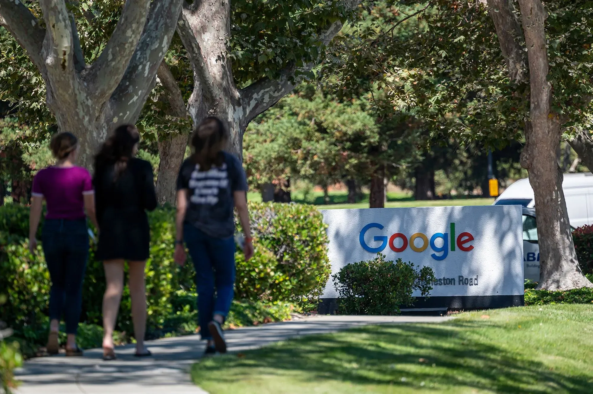 مجموعة من النساء يسيرون بالقرب من علامة جوجل في الحرم الجامعي، مما يعكس دعم النساء في مجال التكنولوجيا وتحدياتهن بعد إلغاء برنامج "صانعات التكنولوجيا النسائية".