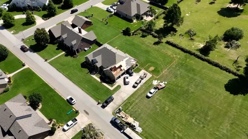 منظر جوي لحي سكني في باراغولد، أركنساس، يظهر منازل تضررت من إعصار، مع وجود سيارات في الشارع وأثاث متروك في الفناء.