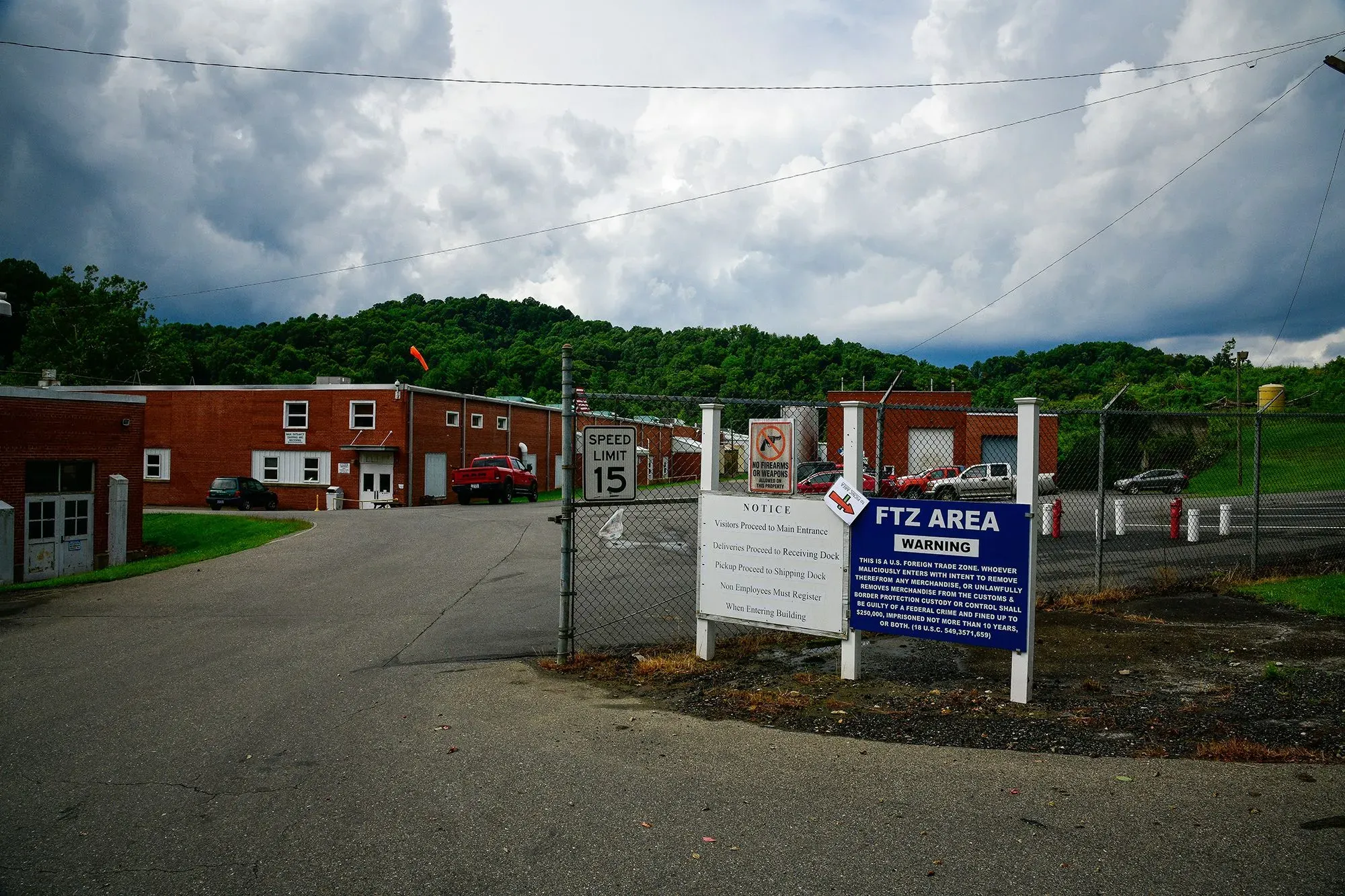 مدخل منطقة التجارة الحرة (FTZ) مع لافتة تحذيرية، وتظهر المباني المحيطة بها والجبال في الخلفية، مما يعكس أهمية هذه المناطق في تخزين السلع.