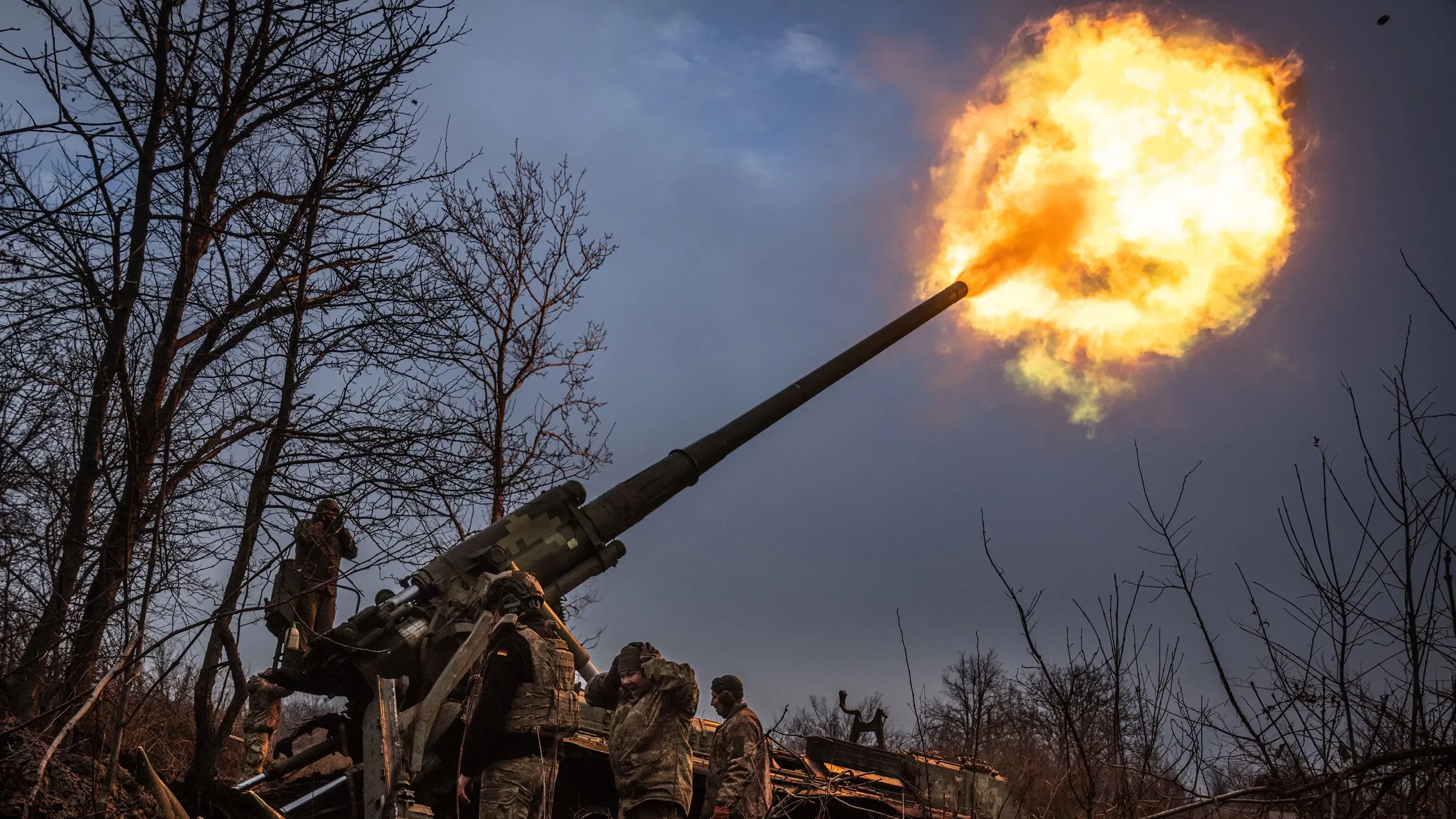 جنود أوكرانيون يقومون بإطلاق قذائف من مدفعية ثقيلة في ساحة المعركة، مع تصاعد النيران والدخان في السماء، مما يعكس التوترات المستمرة في النزاع.