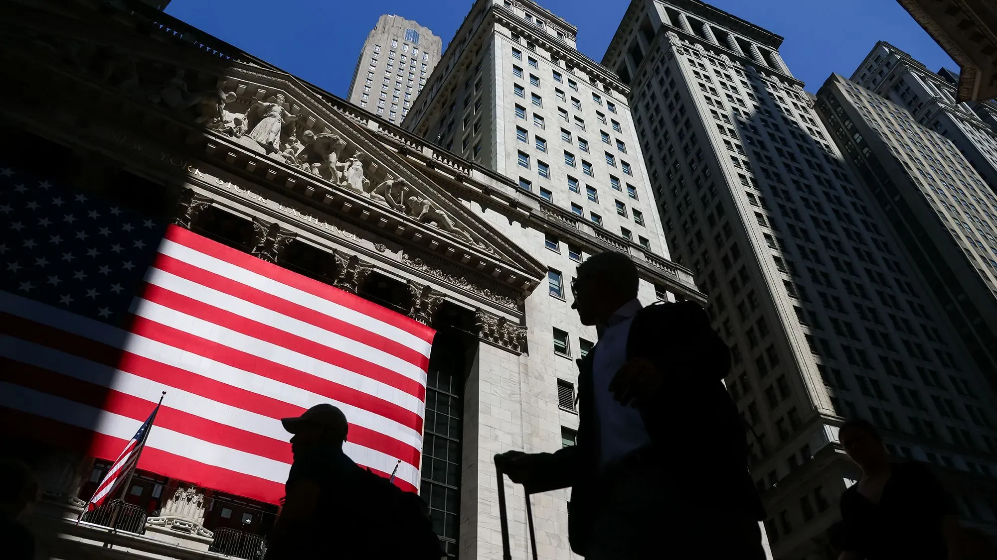 واجهة بورصة نيويورك مع علم الولايات المتحدة الكبير، بينما يتجول المستثمرون في الشارع، مع تزايد التفاؤل بشأن الأسواق المالية.