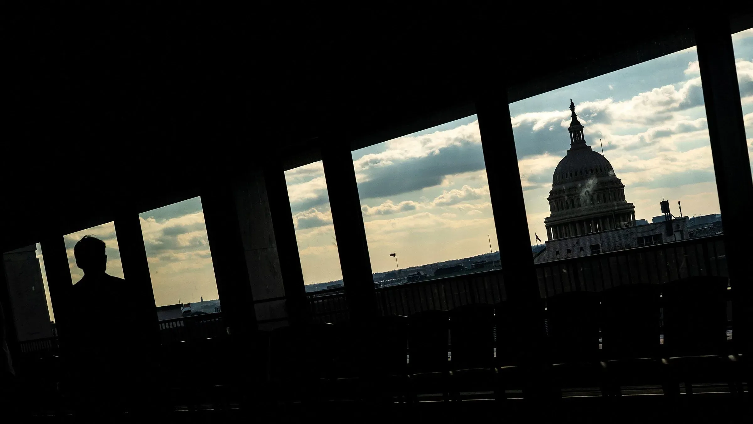 ظل شخص يقف في الظل أمام نوافذ تطل على مبنى الكابيتول الأمريكي، مما يعكس التوترات السياسية في الانتخابات النصفية القادمة.