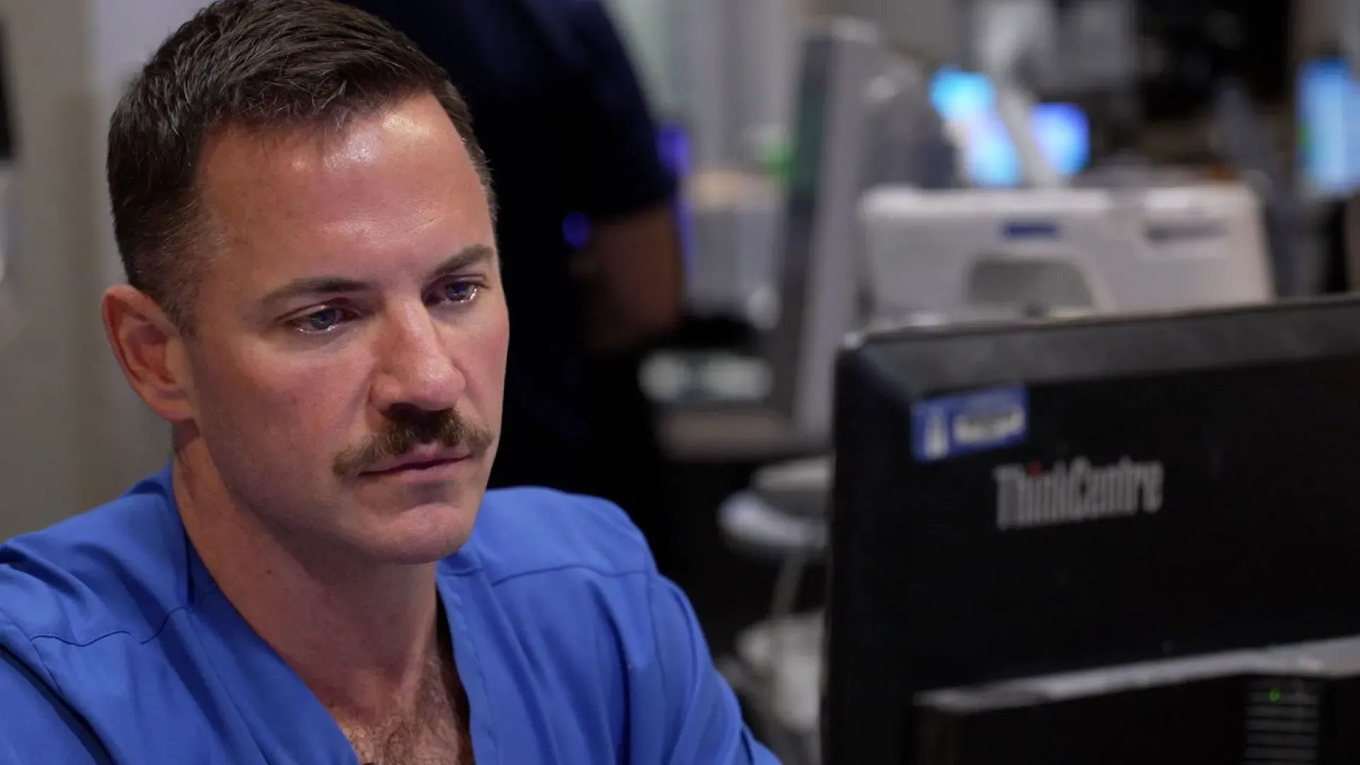 رجل في زي طبي يجلس أمام جهاز كمبيوتر في بيئة طبية، يبدو عليه التركيز والاهتمام، مما يعكس التحديات في مواجهة العنف المسلح في شيكاغو.