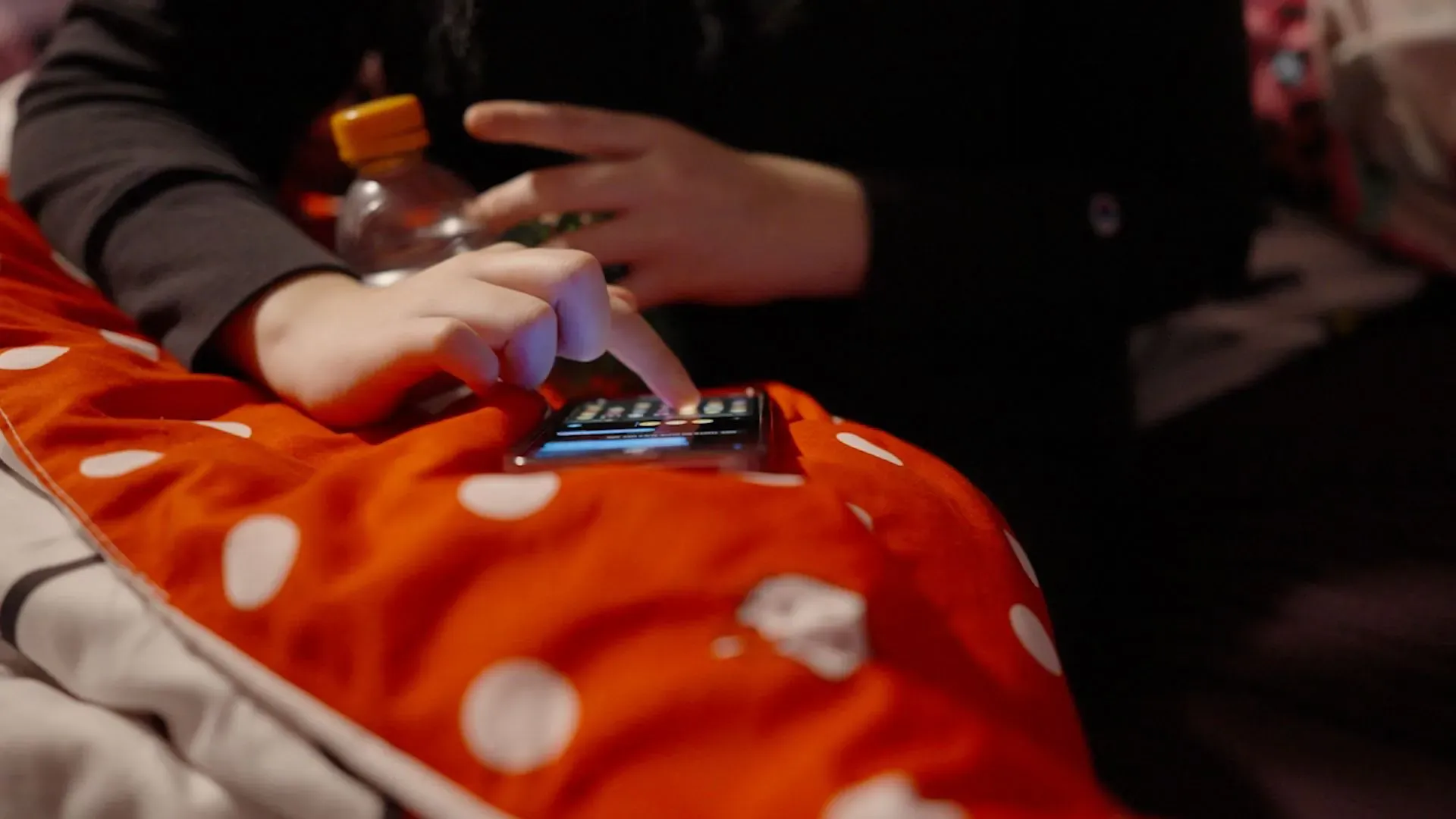 يد تظهر يد شابة تلمس شاشة هاتف ذكي على وسادة حمراء مزينة بنقاط بيضاء، تعكس انغماس الشباب في ثقافة "مجتمع الجريمة الحقيقية".