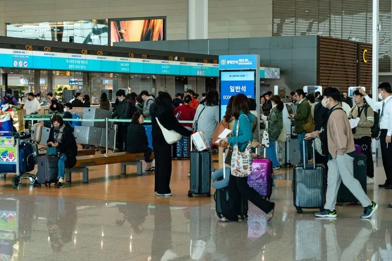 تظهر الصورة مشهدًا مزدحمًا في مطار مع مسافرين ينتظرون في طوابير أمام مكاتب تسجيل الوصول، مما يعكس حركة السفر المتزايدة.