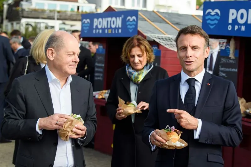 ماكرون وميرتس يتبادلان الحديث أثناء تناول الطعام في حدث رسمي، يعكسان التعاون الفرنسي الألماني.