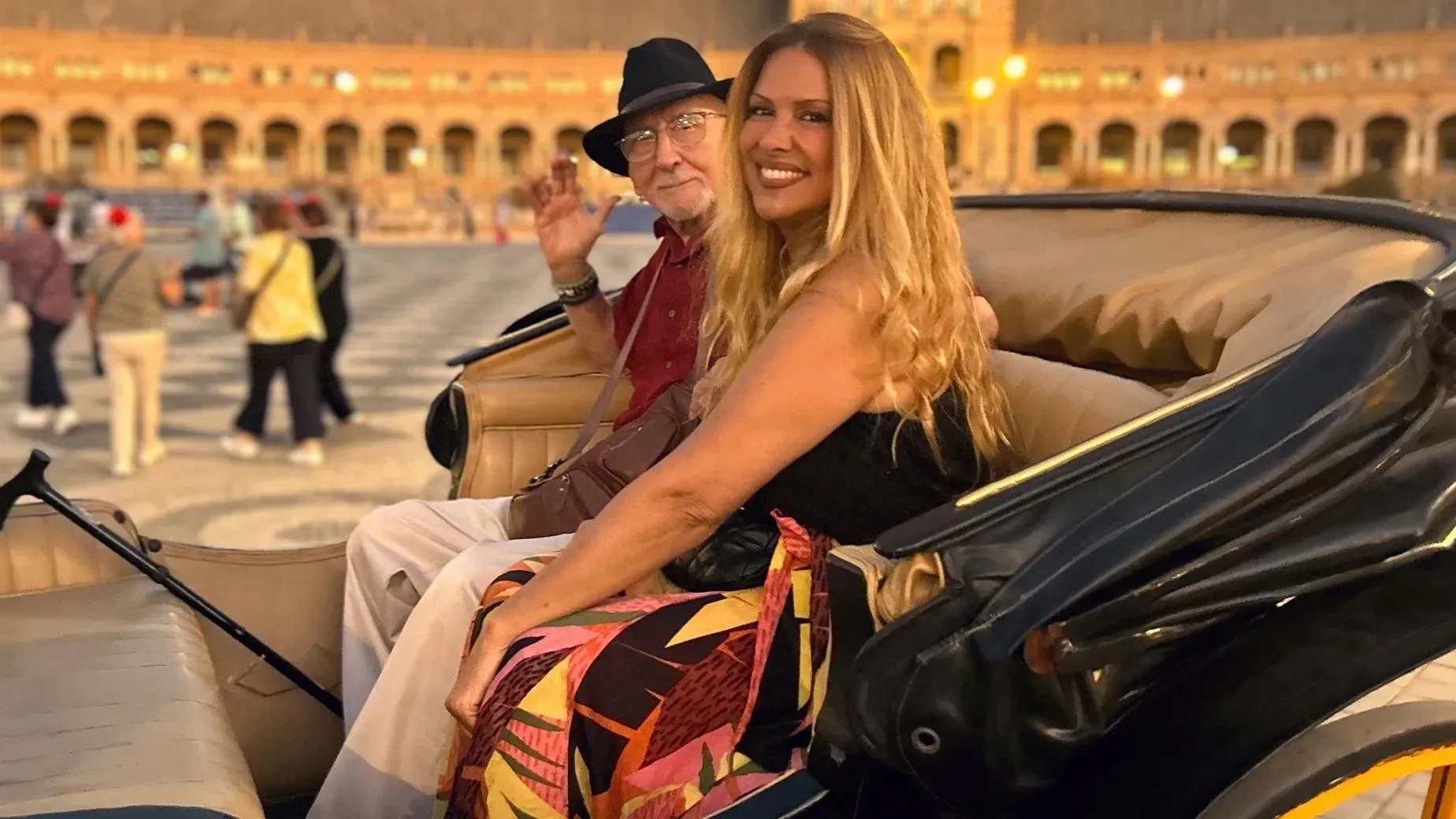 كارينا نوفو ووالدها يجلسان معًا في عربة، مع خلفية معمارية جميلة، يعبران عن بداية جديدة في إسبانيا بعد تحديات حياتية.