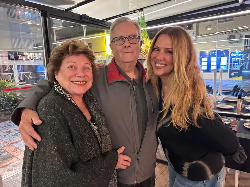 صورة لعائلة مكونة من ثلاثة أفراد، حيث تقف امرأة شابة مع والدها وامرأة مسنّة في مطعم، تعكس لحظة سعيدة من التقاء الأسرة.