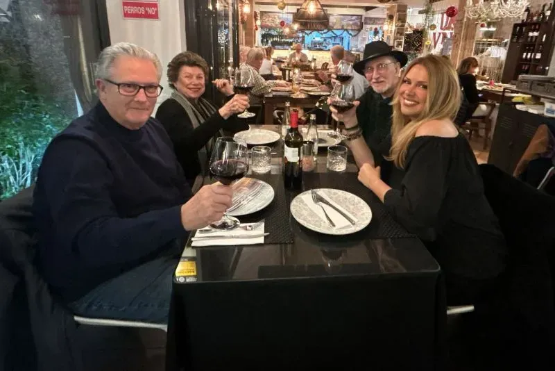 مجموعة من الأشخاص يجلسون حول طاولة في مطعم، يحتفلون معًا بكؤوس النبيذ، مع أجواء مريحة ومشرقة.