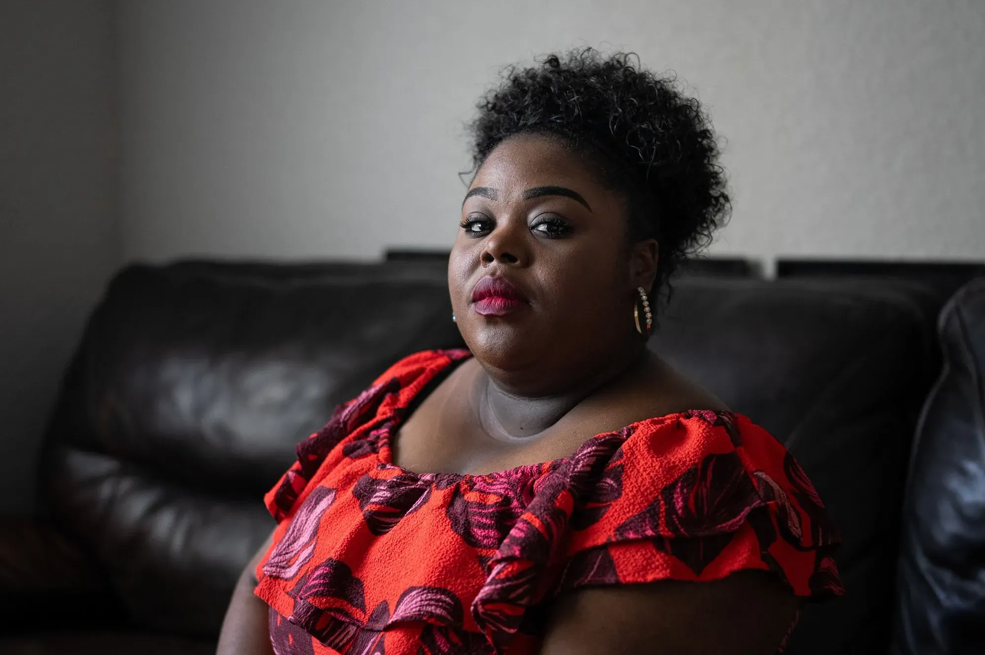 امرأة ذات بشرة داكنة ترتدي فستانًا مزخرفًا بالألوان الزاهية، تجلس على أريكة، تعبر عن مشاعر القوة والتحدي في سياق قضايا حقوق المرأة والولادة.