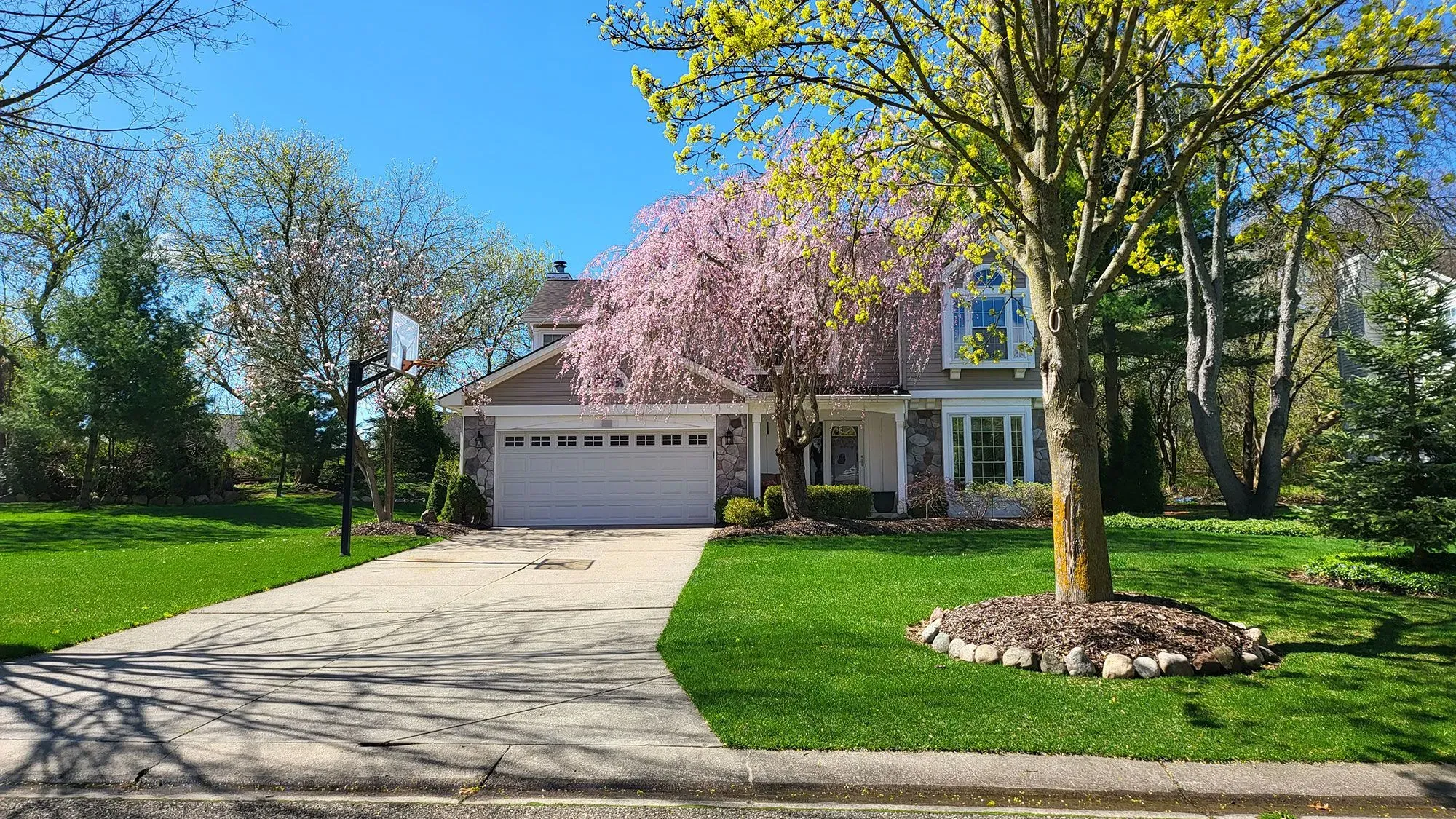 منزل جميل في كلاركستون، ميشيغان، محاط بأشجار مزهرة وحديقة خضراء، يعكس تجربة بيع منزل من قبل المالك.