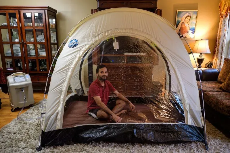 رجل يجلس في خيمة داخل غرفة معيشة، محاط بجهاز لتوليد غاز الزينون، استعدادًا لتسلق قمة إيفرست.