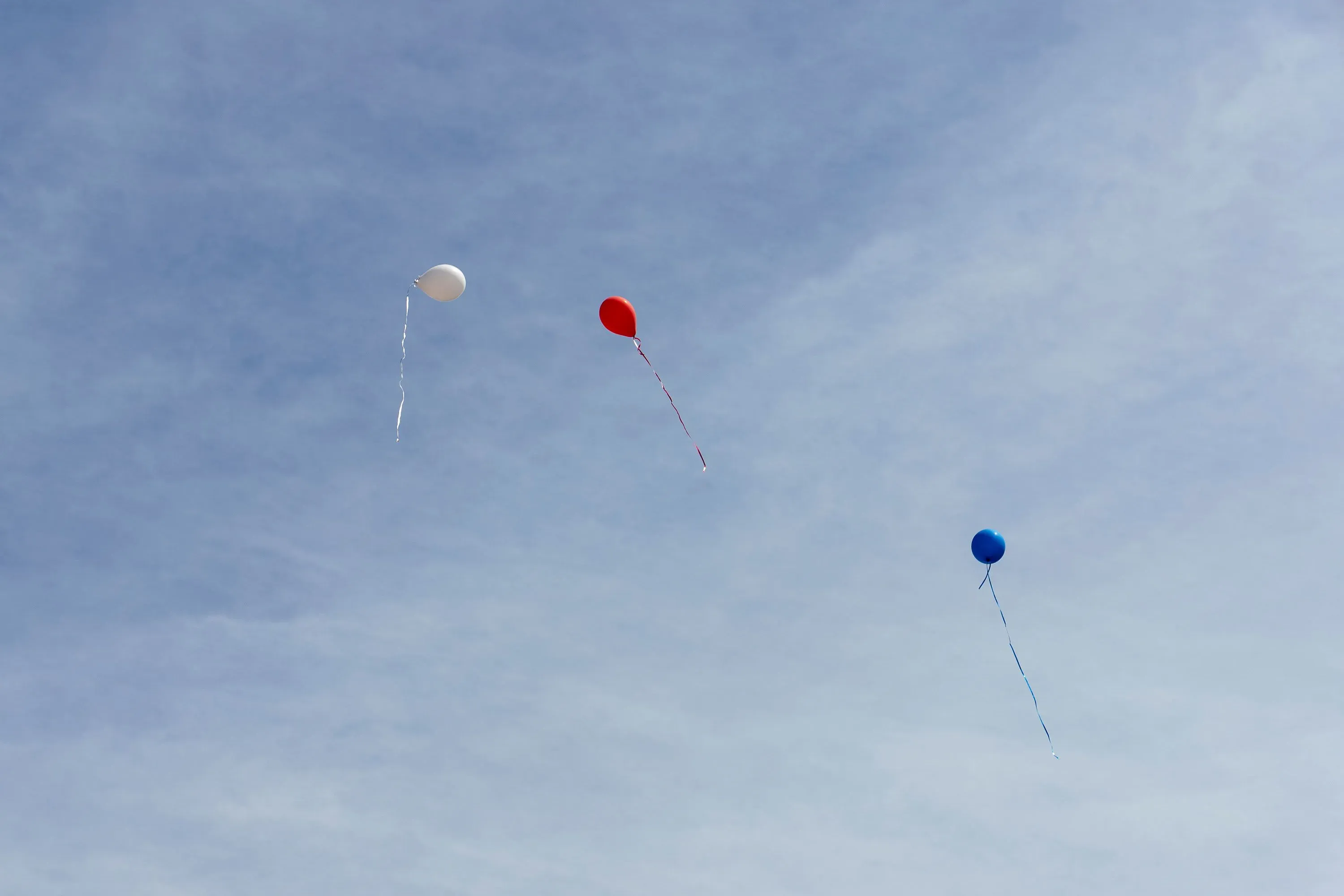 ثلاثة بالونات ملونة (أحمر، أزرق، أبيض) تطفو في السماء الزرقاء، تعكس شعور الأمل والتحديات التي يواجهها المهاجرون.