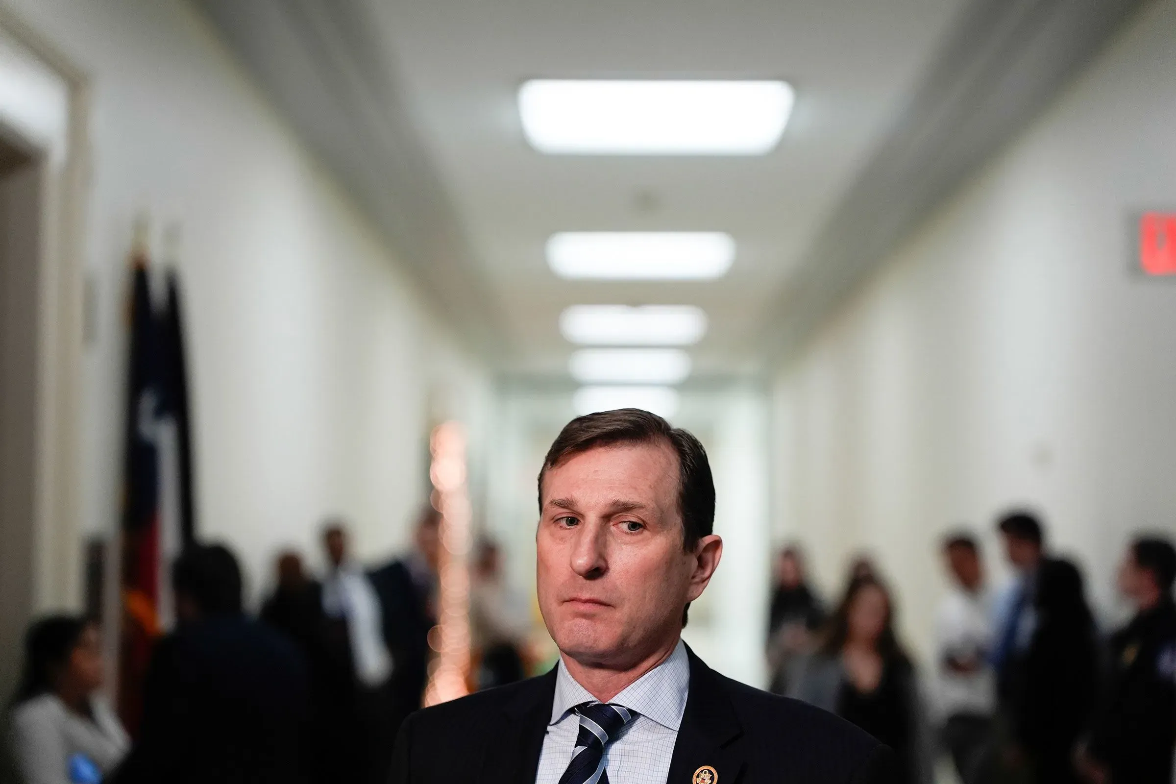 النائب دان جولدمان يقف في ممر الكونغرس، مع خلفية تضم أعلام وناس يتحدثون، في إطار معركة انتخابية حادة.