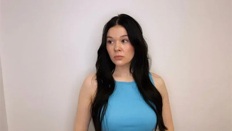 امرأة ذات شعر أسود طويل ترتدي قميصًا أزرق، تبدو مشوشة وتعبر عن القلق. الصورة تعكس المخاوف المتزايدة بين حاملي البطاقة الخضراء في الولايات المتحدة.