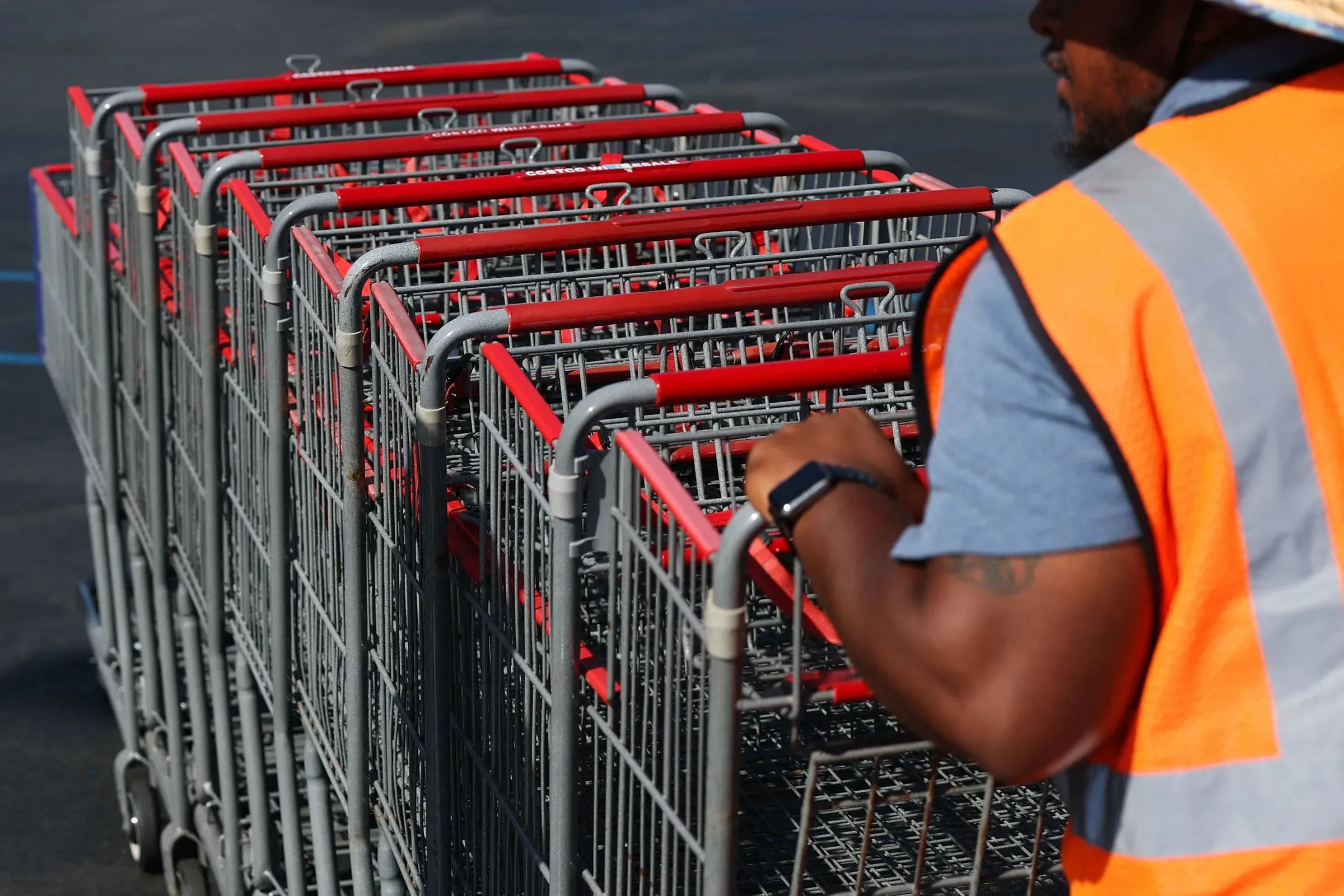 عامل يرتدي سترة برتقالية يقوم بإعادة ترتيب عربات التسوق في موقف سيارات، مما يعكس نشاط العمل الإضافي وتأثيره على الضرائب.