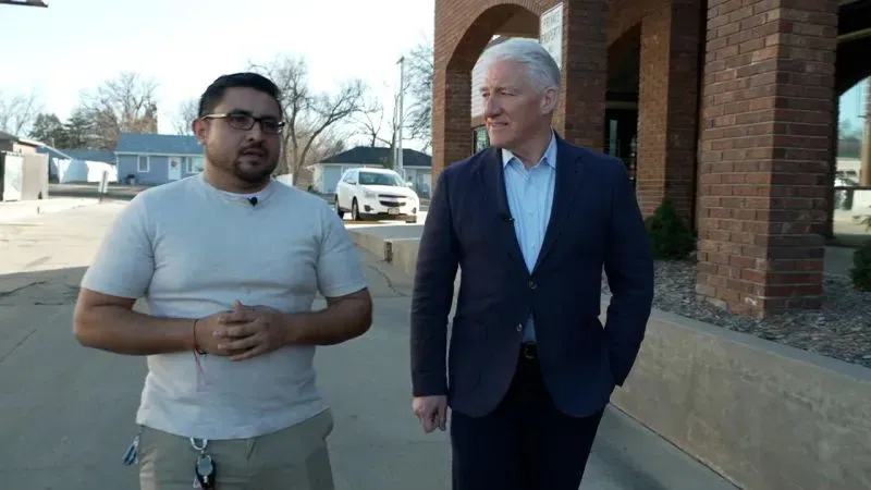 رجلان يتحدثان في أحد شوارع نبراسكا، مع منازل وخدمات خلفهما، تعكس قلق المهاجرين في ظل السياسات الحالية.