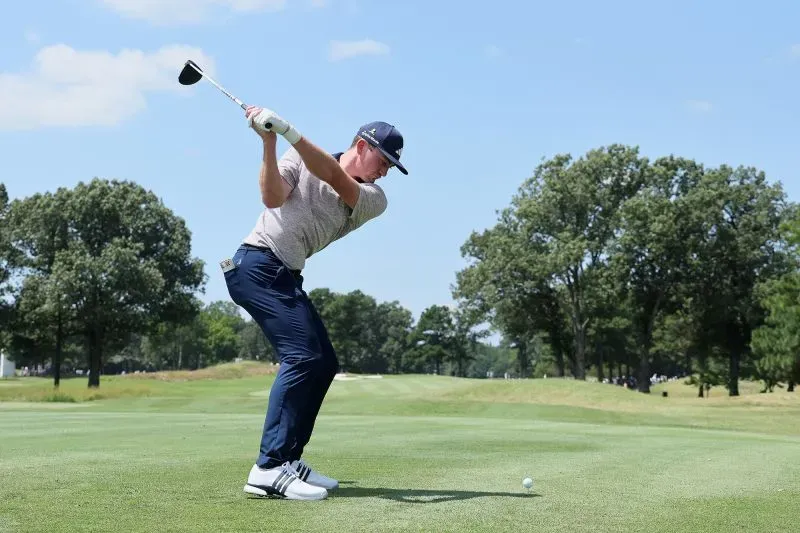 نيك دنلاب يستعد لضرب كرة الغولف في ملعب، حيث يظهر التركيز والحماس في أدائه، محاطًا بأشجار خضراء في يوم مشمس.