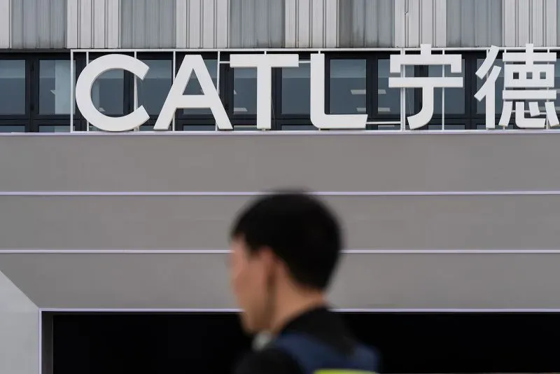 شعار شركة CATL يظهر في موقعها، مع شخص يمر بجانبه، مما يعكس التوسع العالمي للشركة في صناعة بطاريات السيارات الكهربائية.