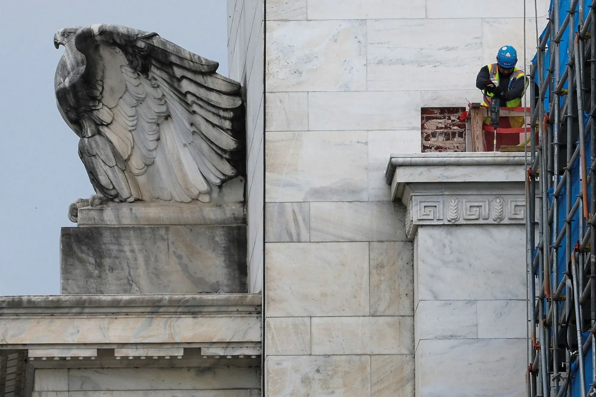 عمال يجرون أعمال ترميم على مبنى حكومي، مع وجود نسر منحوت على الواجهة، مما يعكس أهمية الاقتصاد والسياسات التجارية.