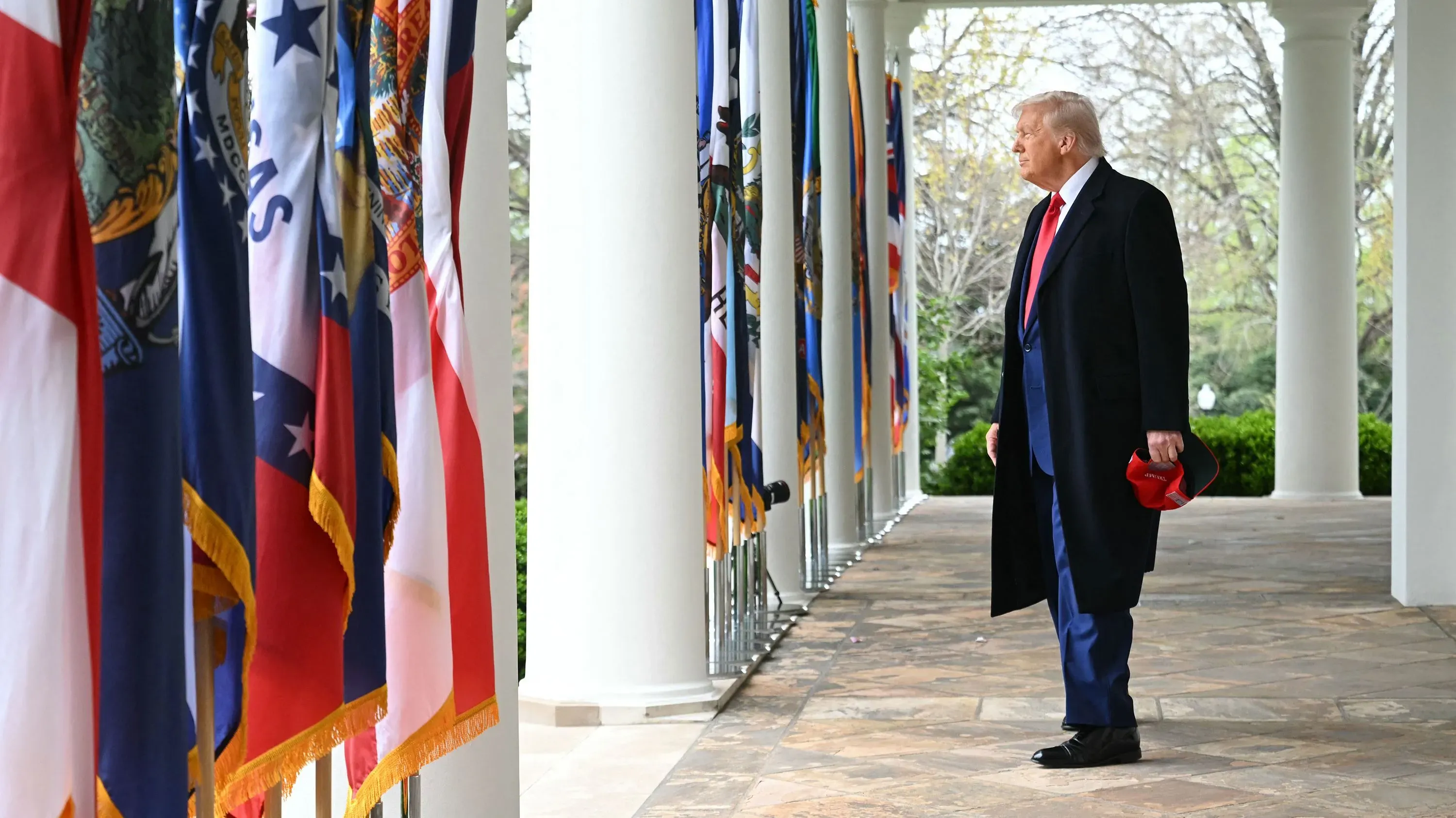 ترامب يقف في الردهة مع الأعلام خلفه، محذراً من انهيار السوق إذا خسرت هاريس الانتخابات. تعكس الصورة أجواء التوتر السياسي والاقتصادي.