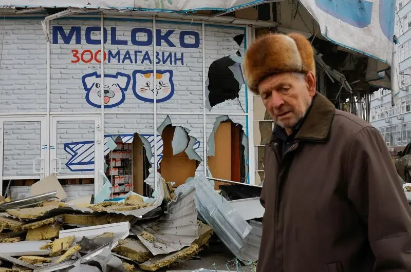 رجل مسن يرتدي قبعة يقف أمام متجر حيوانات مدمّر في أوكرانيا، حيث تعكس الأضرار آثار الاحتلال الروسي.