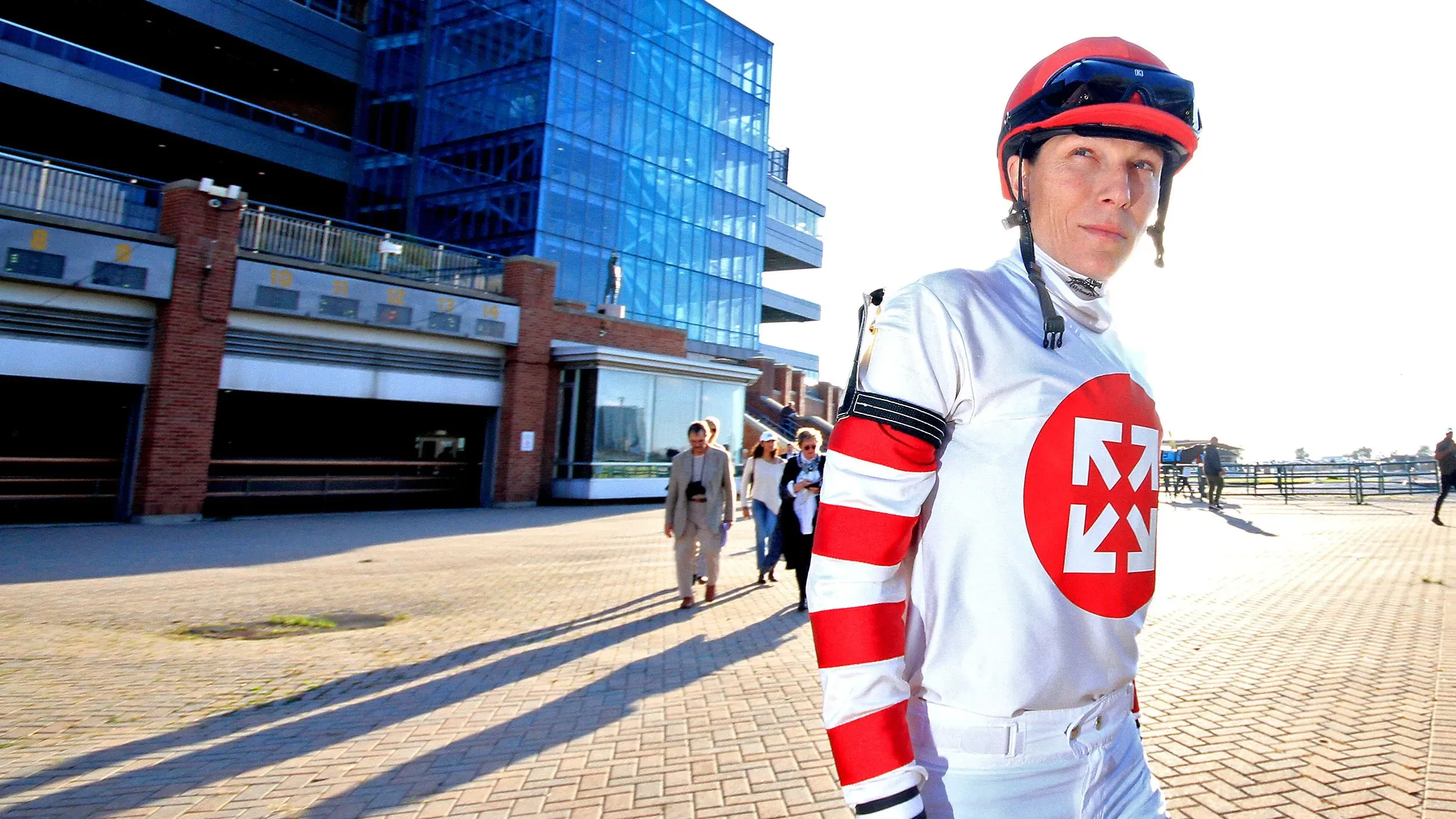 إيما-جاين ويلسون، الفارسة الشهيرة، تسير في مضمار السباق مرتدية زيها الرسمي، تعكس عزمها على التعافي بعد حادث مروع.