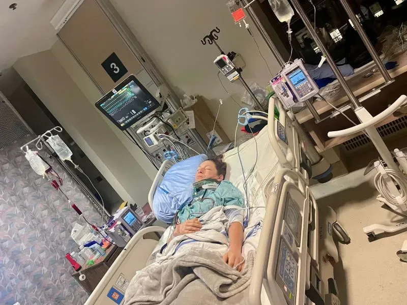 إيما-جاين ويلسون مستلقية على سرير المستشفى، تتلقى الرعاية الطبية بعد إصابتها في حادث سباق خيل، مع أجهزة طبية حولها.