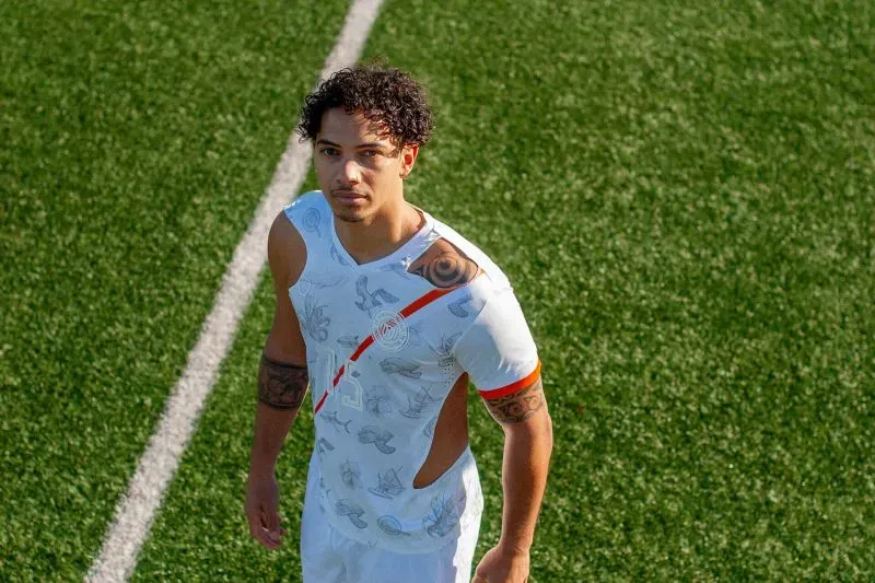 لاعب كرة قدم يرتدي قميصًا جديدًا مستوحى من ثقافة جزر مارشال، يظهر في ملعب عشبي، يعكس التحديات البيئية التي تواجه البلاد.