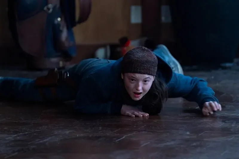 إيلي تتسلل على الأرض في كوخ، تعبيرها يظهر الخوف والقلق، في لحظة حاسمة من الحلقة الأخيرة من مسلسل "آخرنا".