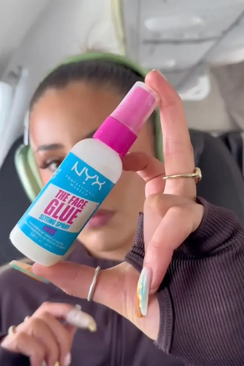 زائرة في الطائرة تظهر زجاجة بخاخ تثبيت المكياج من علامة NYX، تعكس صيحة العناية بالبشرة والجمال أثناء الرحلات الجوية.