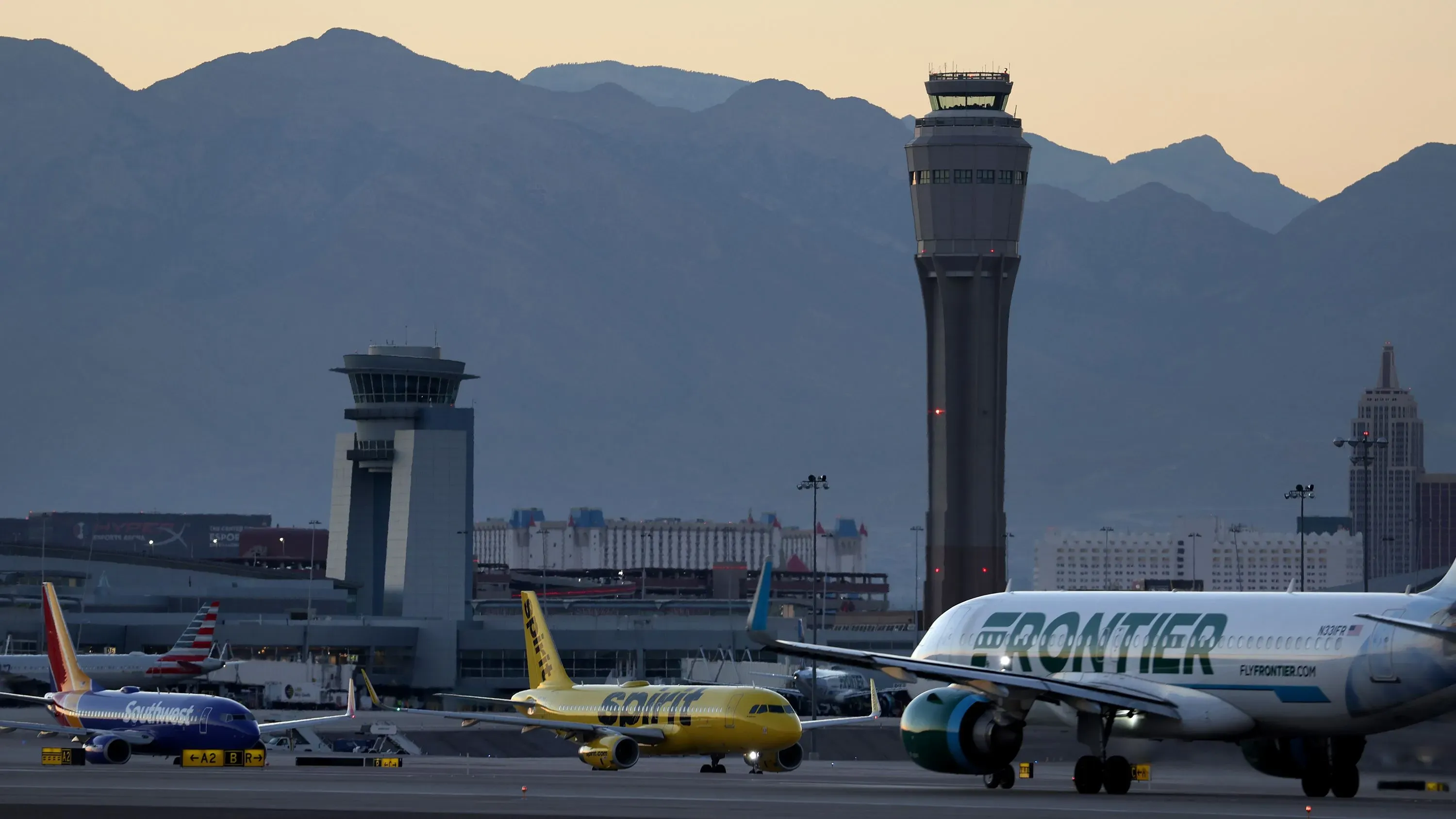 مطار هاري ريد الدولي في لاس فيغاس مع طائرات تجارية على المدرج، خلفه برج المراقبة وجبال في الأفق، يشير إلى مخاطر التصادمات الجوية.