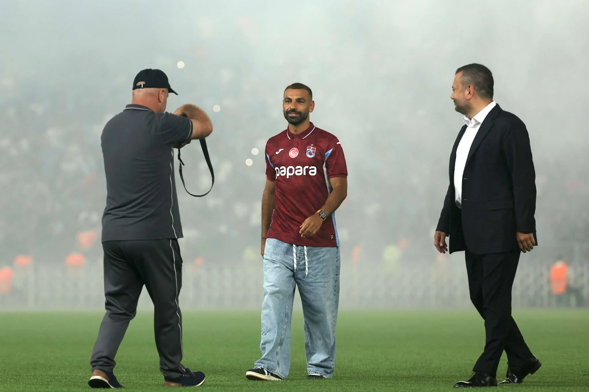 محمد صلاح يرتدي قميص طرابزون سبور الجديد وسط أجواء احتفالية في الملعب مع حضور رسمي وتصوير إعلامي.