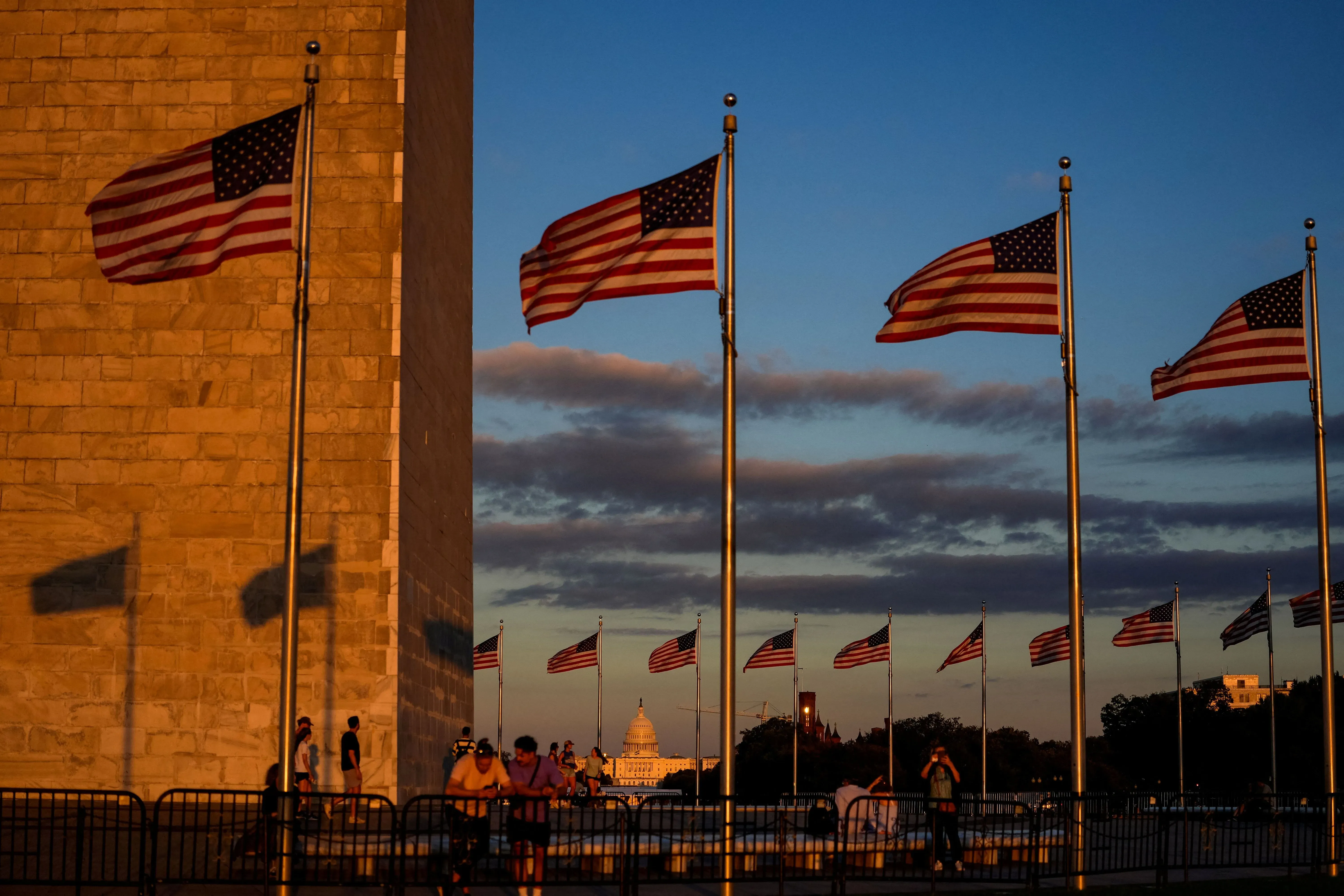 أعلام أمريكية ترفرف في المساء بالقرب من نصب واشنطن، مع منظر لبرلمان الولايات المتحدة في الخلفية، تعبيرًا عن الأحداث السياسية الراهنة.