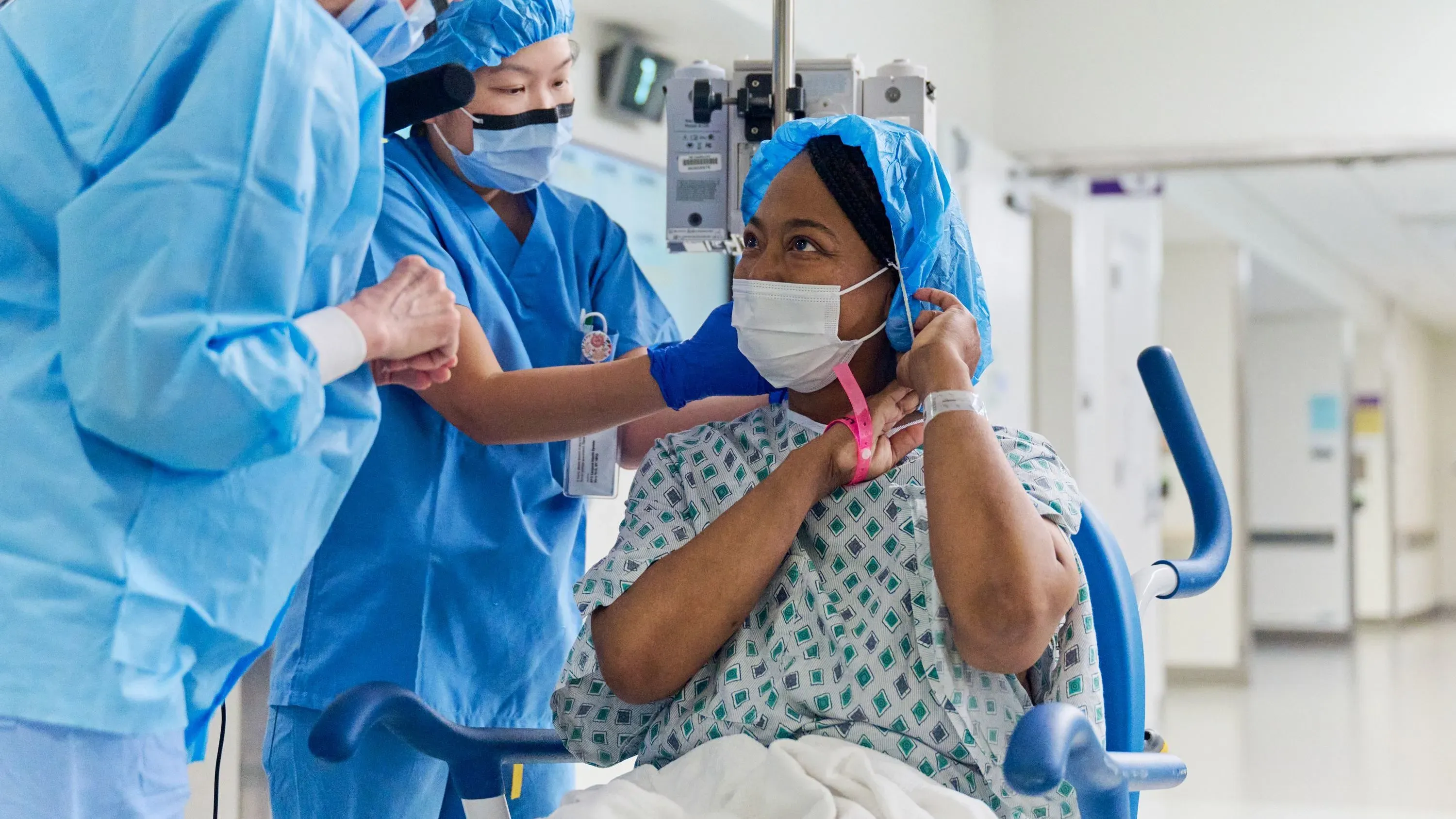 امرأة ترتدي زي المستشفى وتستعد لعملية زراعة كلية خنزير، محاطة بمقدمي الرعاية الصحية في بيئة طبية.