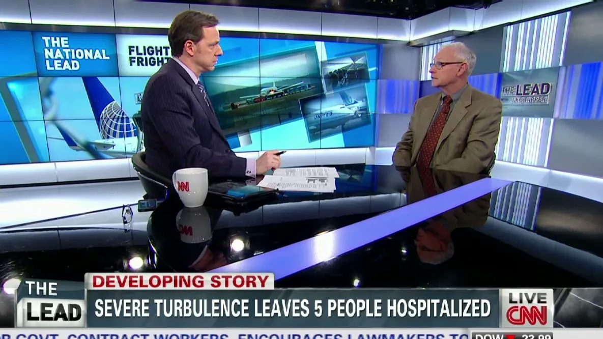 مقابلة تلفزيونية تتناول المخاطر الصحية لربط حزام الأمان حول الكاحلين أثناء الرحلات الجوية، مع التركيز على سلامة الركاب.